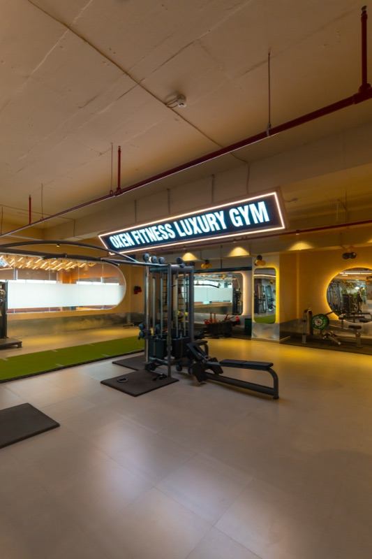 The gym floor at Oxen: a cable machine and a bench under the lit ‘Oxen Fitness Luxury Gym’ sign